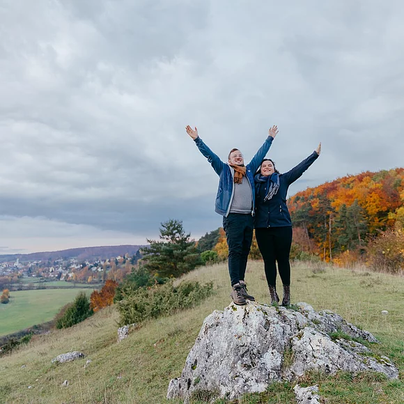 Ein Pärchen unterwegs auf der Heide bei Harburg vor einem herbstlich buntem Wald. Links im Hintergrund sieht man die Wörnitz und die Stadt Harburg.