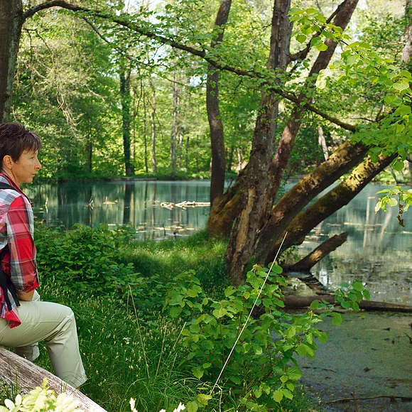 Eine Wanderin sitzt am idyllischen Doosweiher und blickt auf das Wasser.
