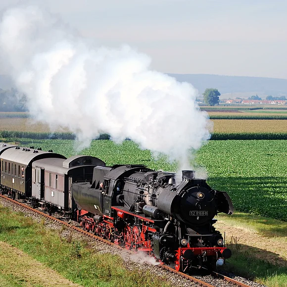 Eine Dampflokomotive mit Waggons fährt rauchend durch das Ries