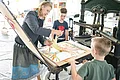 Die Leiterin des KunstMuseums führt zwei Jungs den Bilddruck mit einer alten Maschine vor.