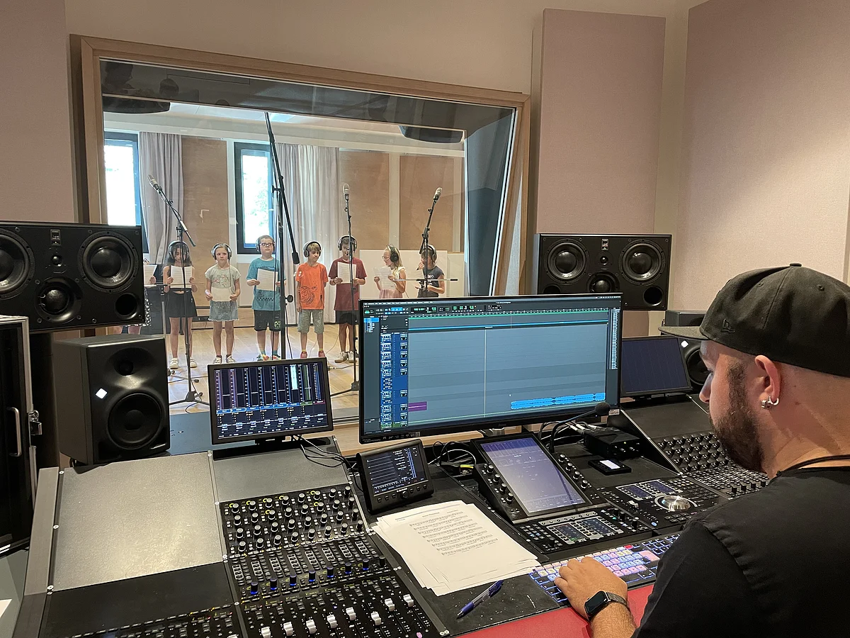 Drei Jungen stehen an Mikrofonen in einem Aufnahmestudio.