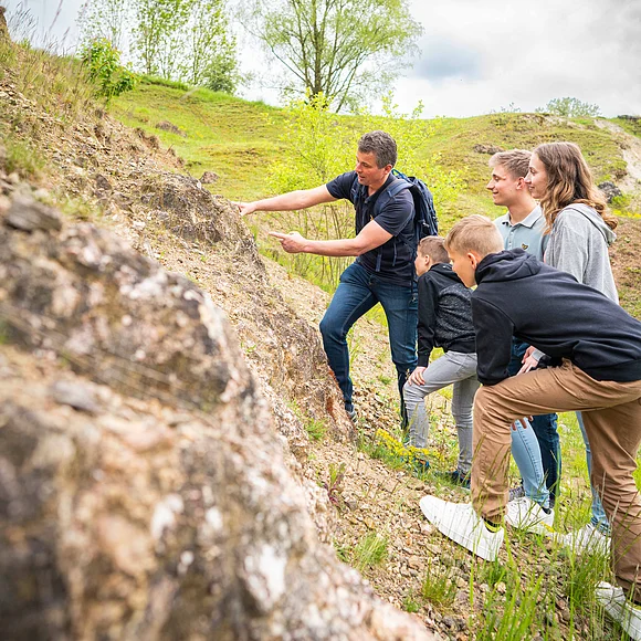 Ein Mann zeigt einer Gruppe von Kindern und Jugendlichen einen geologischen Aufschluss.