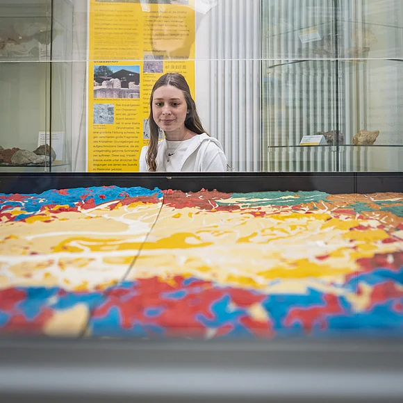 Geopark-Ries Juni 2022 Ein Mädchen betrachtet ein bunt eingefärbtes Modell einer Landschaft in einer Vitrine. Im Hintergrund ist eine gelbe Informationstafel zu sehen.