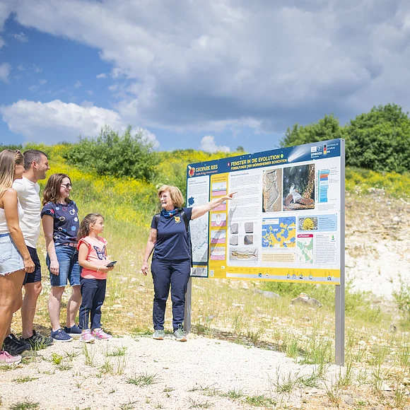 Eine Geopark Ries Führerin zeigt einer kleinen Gruppe Personen eine Informationstafel.