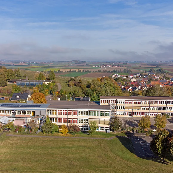 Hinter mehreren länglichen dreistöckigen Gebäuden dehnt sich die weite Landschaft des Rieskraters aus.