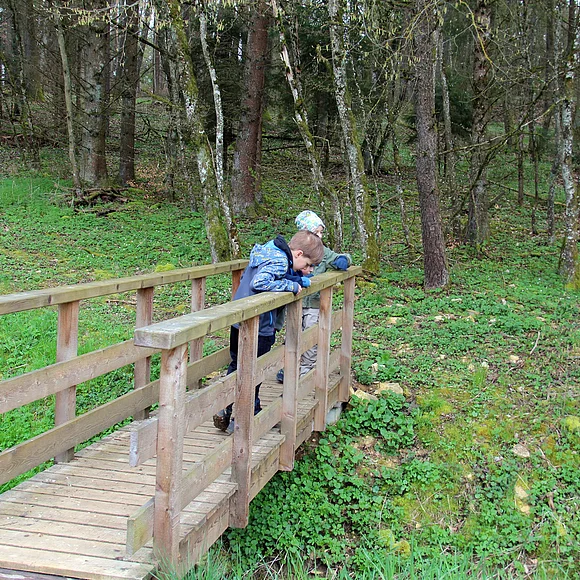 Zwei Kinder stehen auf einer Holzbrücke, die über einen Graben führt.