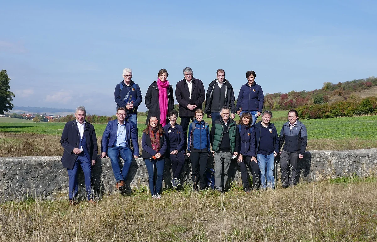 Gruppenfoto der Beteiligten bei der UNESCO-Bereisung auf einer Wiese, wobei ein Teil der Personen auf einer niedrigen Mauer steht.
