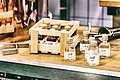 In einer kleinen Holzkiste und auf Tisch daneben stehen kleine Glasfalschen mit Holzkorken und der Aufschrift "Appl" auf dem Etikett.