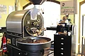 Das Kühlsieb eines großen schwarzen Kaffeerösters enthält viele Kaffeebohnen.