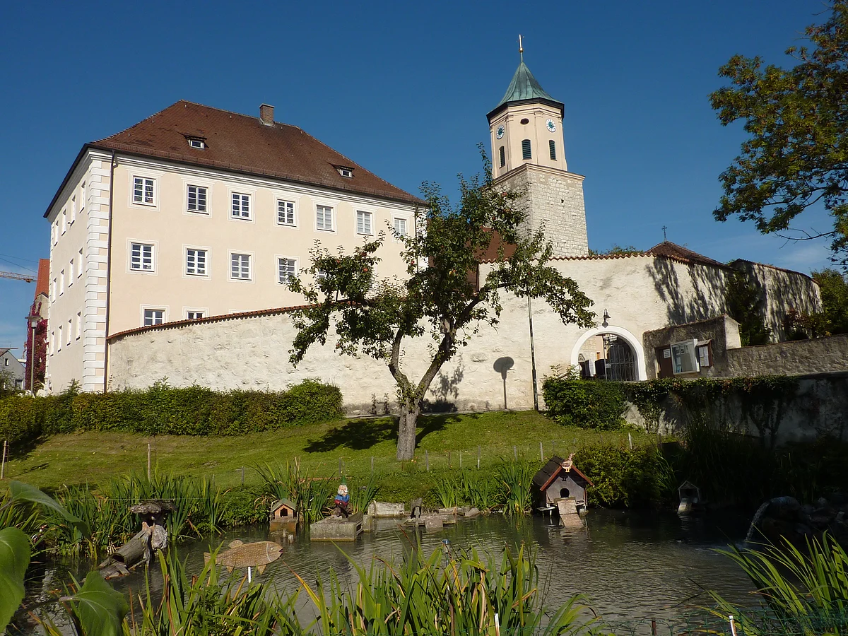 Blick auf das ehemalige Schloss Gosheim mit davor liegendem Weiher. Rechts neben dem Schloss sieht man den Turm der Pfarrkirche Mariä Geburt.