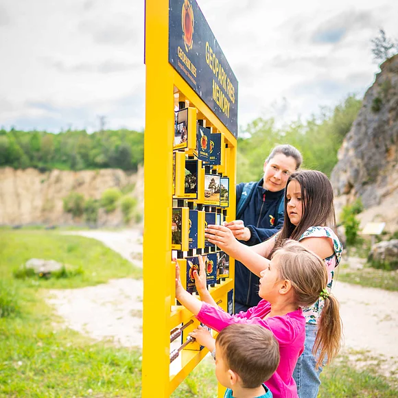 Eine Frau und drei Kinder spielen ein Outdoor-Memory.