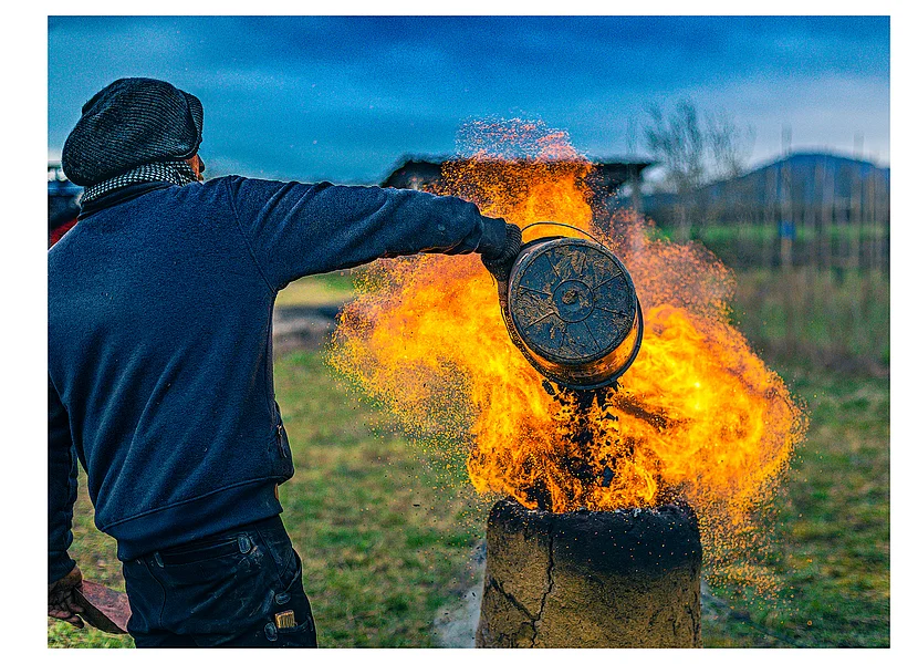 Ein Mann befüllt einen einen lodernden, historischen Rennofen zur Eisengewinngung.