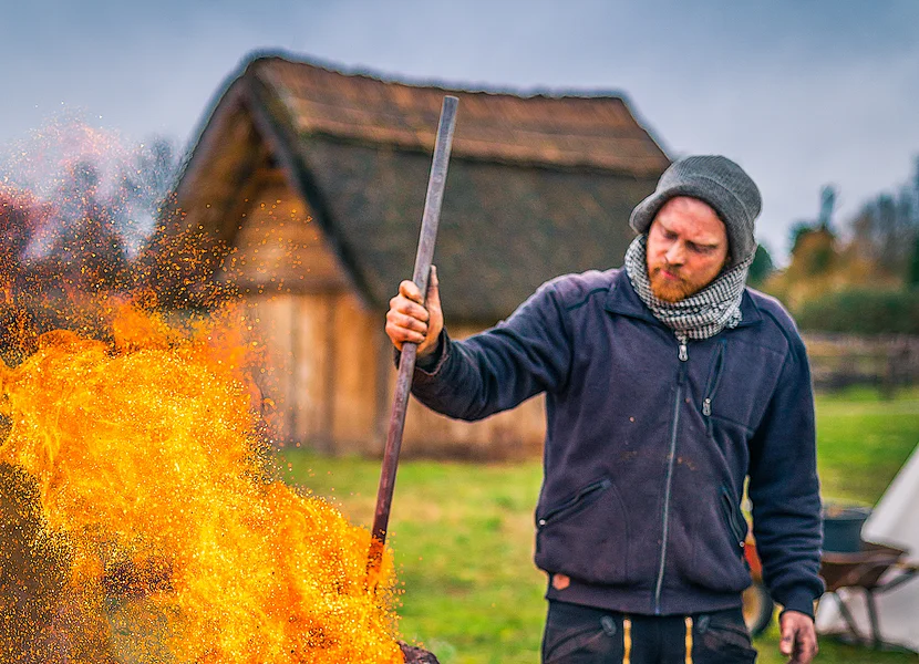 Ein Mann hält das Feuer eines historischen Rennofens zur Eisengewinnung am Brennen.