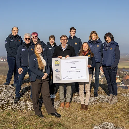 Team Geopark Ries e. V. Gruppenfoto des Teams des Geopark Ries mit der Urkunde der International Union of Geological Sciences. Im Hintergrund erstreckt sich in einer Senke eine weite Landschaft.
