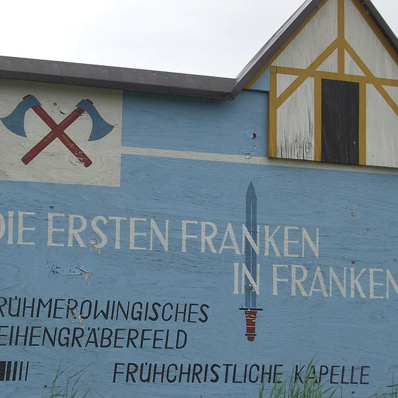 Ein großer hölzerner Wegweise zur rekonstruierten frühchristlichen Kapelle