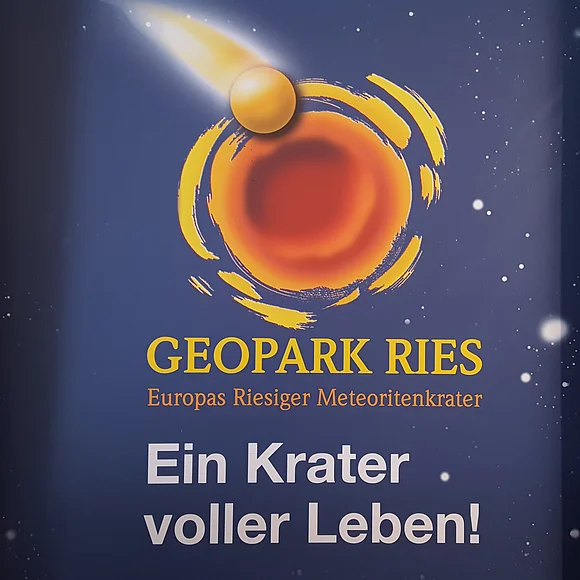 Auf dunkelblauem Hintergrund mit weißen Punkten als Sterne befindet sich das Logo des Geopark Ries und der Schriftzug "Ein Krater voller Leben!".