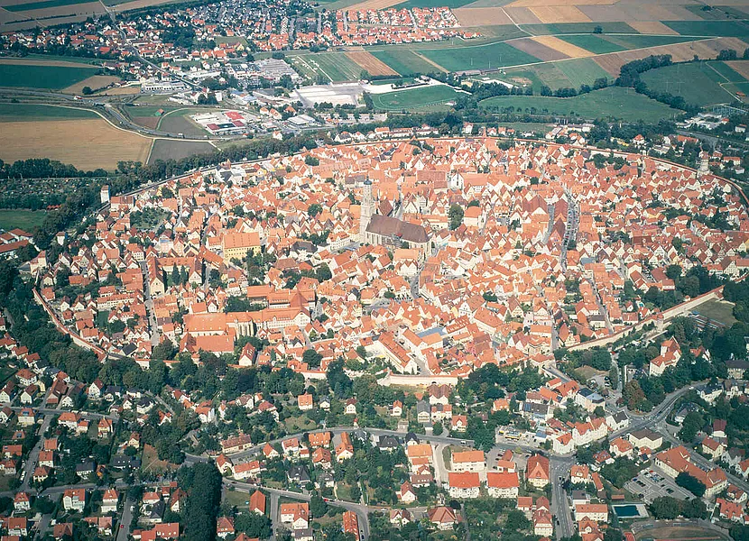 Das Luftbild zeigt die kreisrunde Altstadt von Nördlingen mit dem Kirchturm in der Mitte. Außerhalb der Stadtmauer schließen sich weitere Siedlungen an.