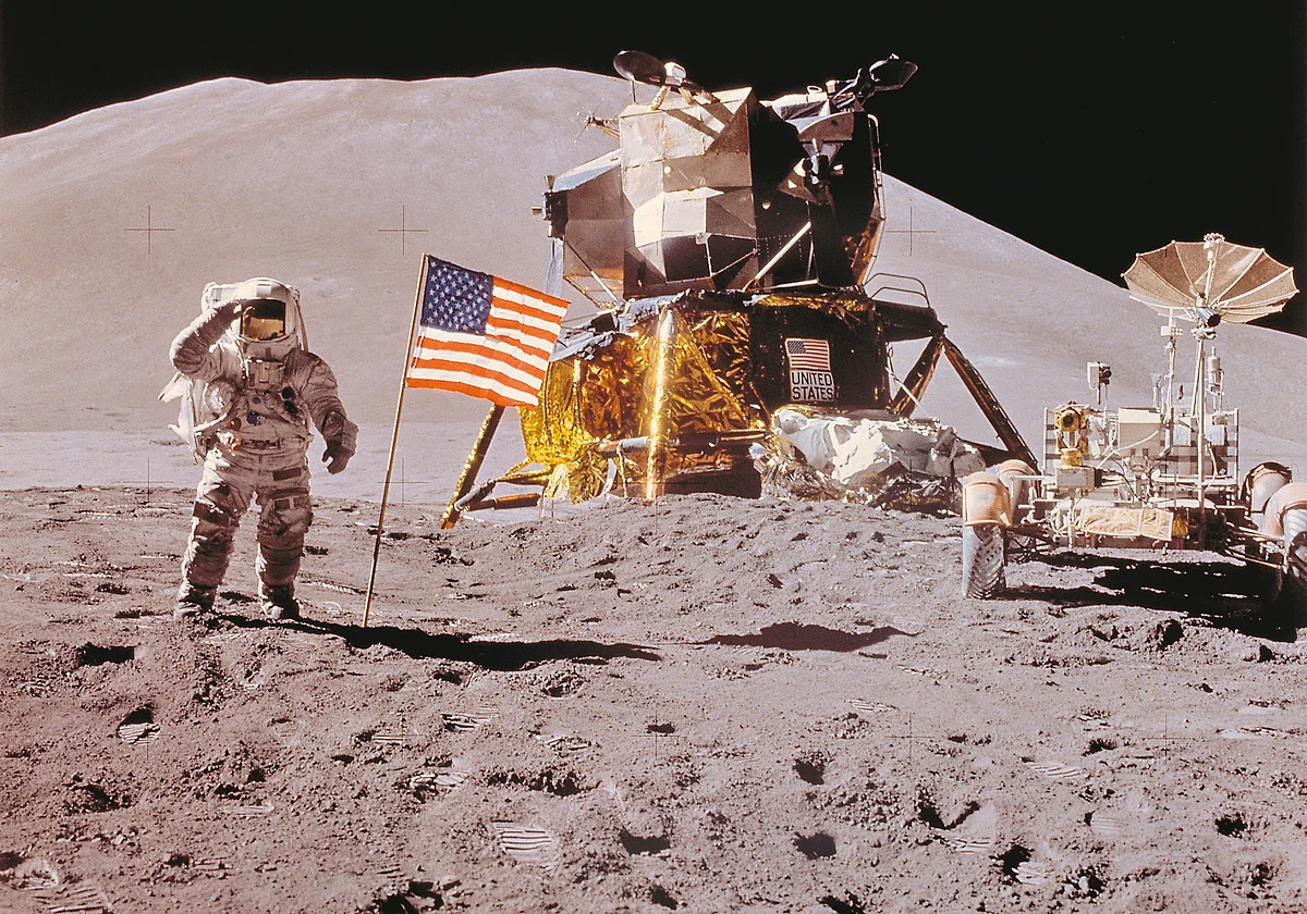 Ein Astronaut steht neben einer USA-Flagge auf der Mondoberfläche. Im Hintergrund sind zwei Mondrover zu sehen.