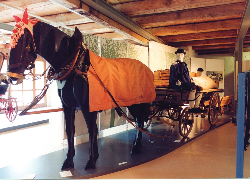 In einem Museum ist eine Pferdefigur vor einen Wagen gespannt, auf dem eine männliche Puppe sitzt.
