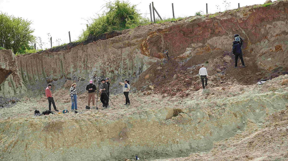 In einem ehemaligen Steinbruch stehen Personen an der rötlichen Felswand. In einiger Entfernung stehen weitere Personen mit einem Stativ.