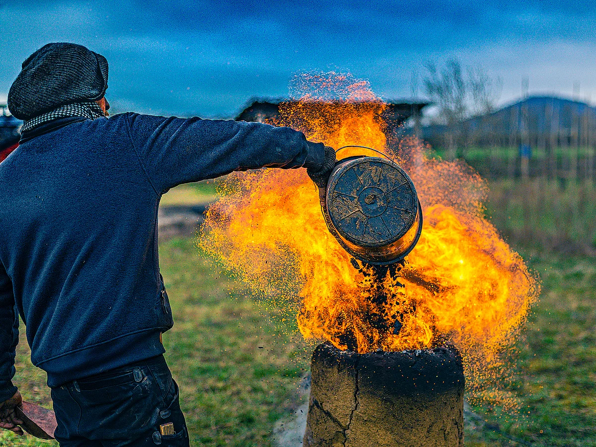 Ein Mann befüllt einen einen lodernden, historischen Rennofen zur Eisengewinngung.