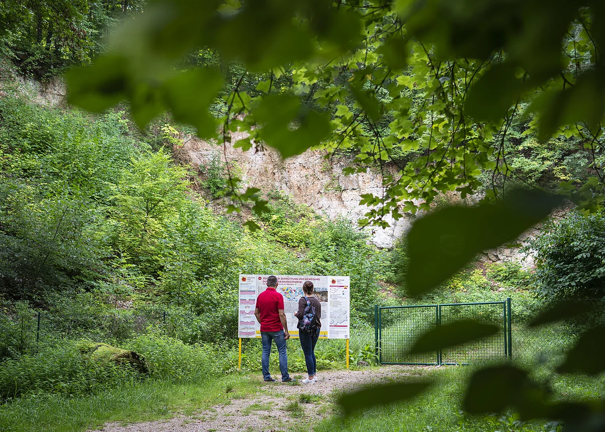 Steinbruch am Geopark Ries Sagenweg 2 Menschen stehen vor der Geopark Ries Tafel des Steinbruchs am Sagenweg bei Wemding.