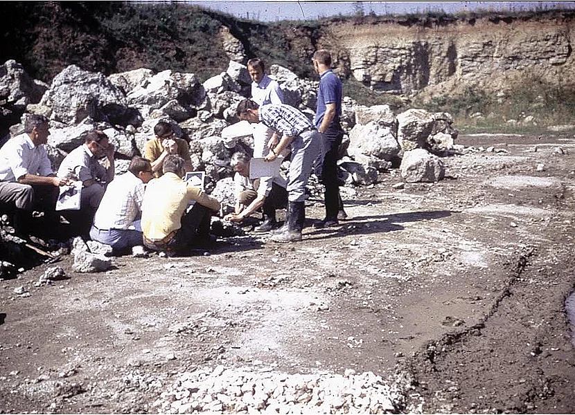 Für die Apollo-Missionen führten amerikanische Astronauten im Ries ein Feldtraining durch. Mehrere Personen sitzen oder stehen neben einem Haufen Gesteinsbruchstücke. Im Hintergrund ist die Felswand eines ehemaligen Steinbruchs zu sehen.