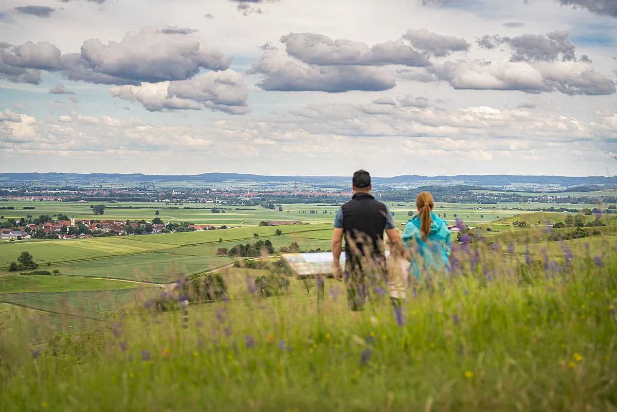 Panoramablick bei Kirchheim am Ries Zwei Personen stehen auf einem Hügel und blicken auf eine weite Landschaft mit Feldern und einem Dorf.
