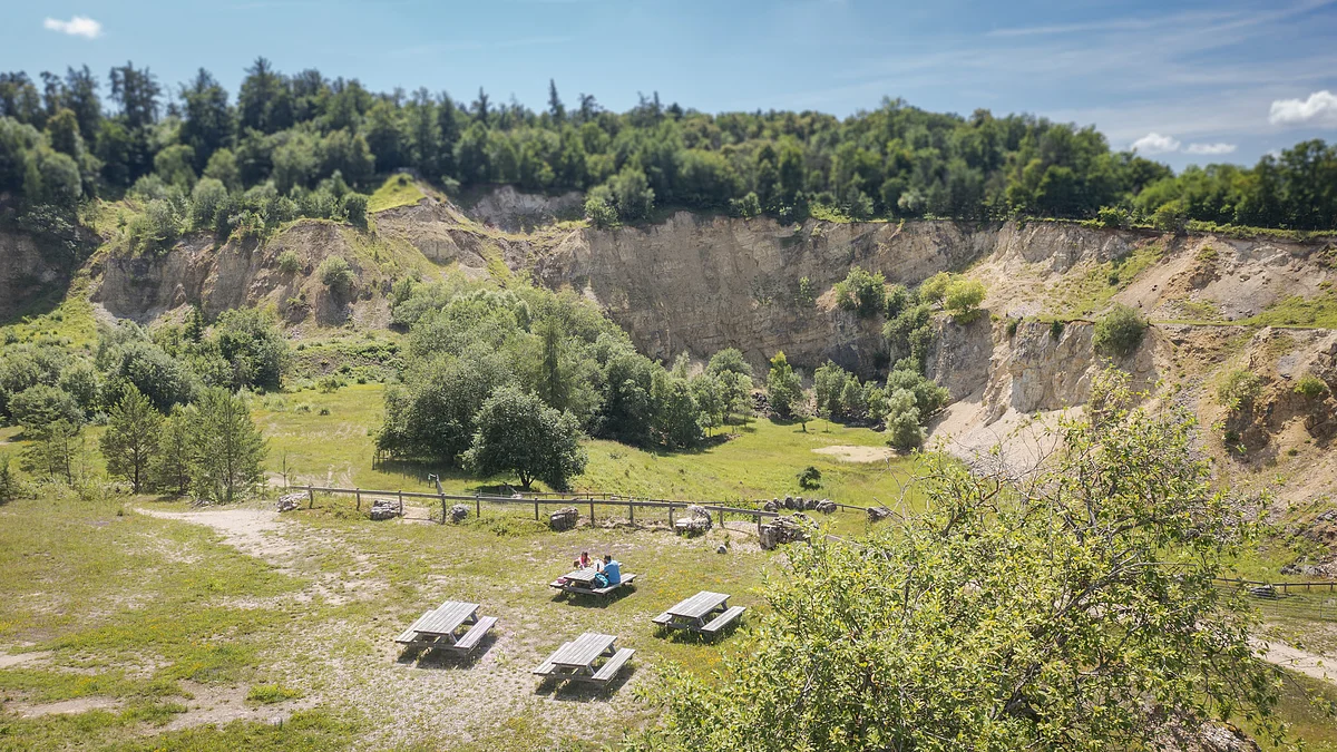 Eine Landschaft mit steilen Felswänden, Bäumen und mehreren Picknicktischen im Vordergrund.