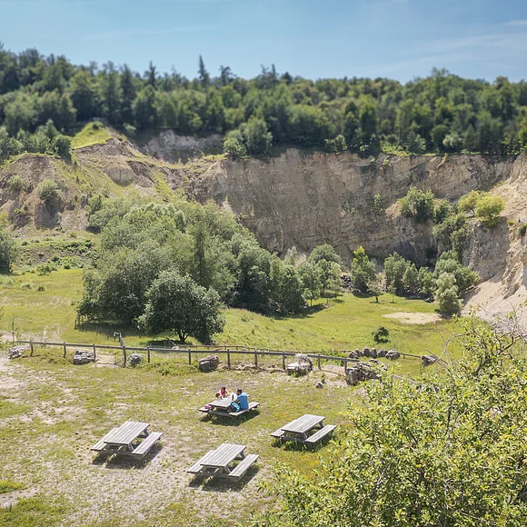 Eine Landschaft mit steilen Felswänden, Bäumen und mehreren Picknicktischen im Vordergrund.