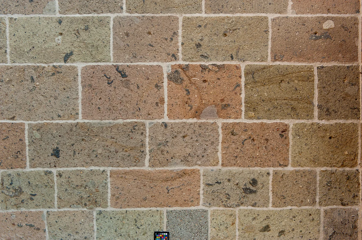 Die glatten rötlichen Steine einer Mauer weisen unregelmäßige schwarze Flecken auf.