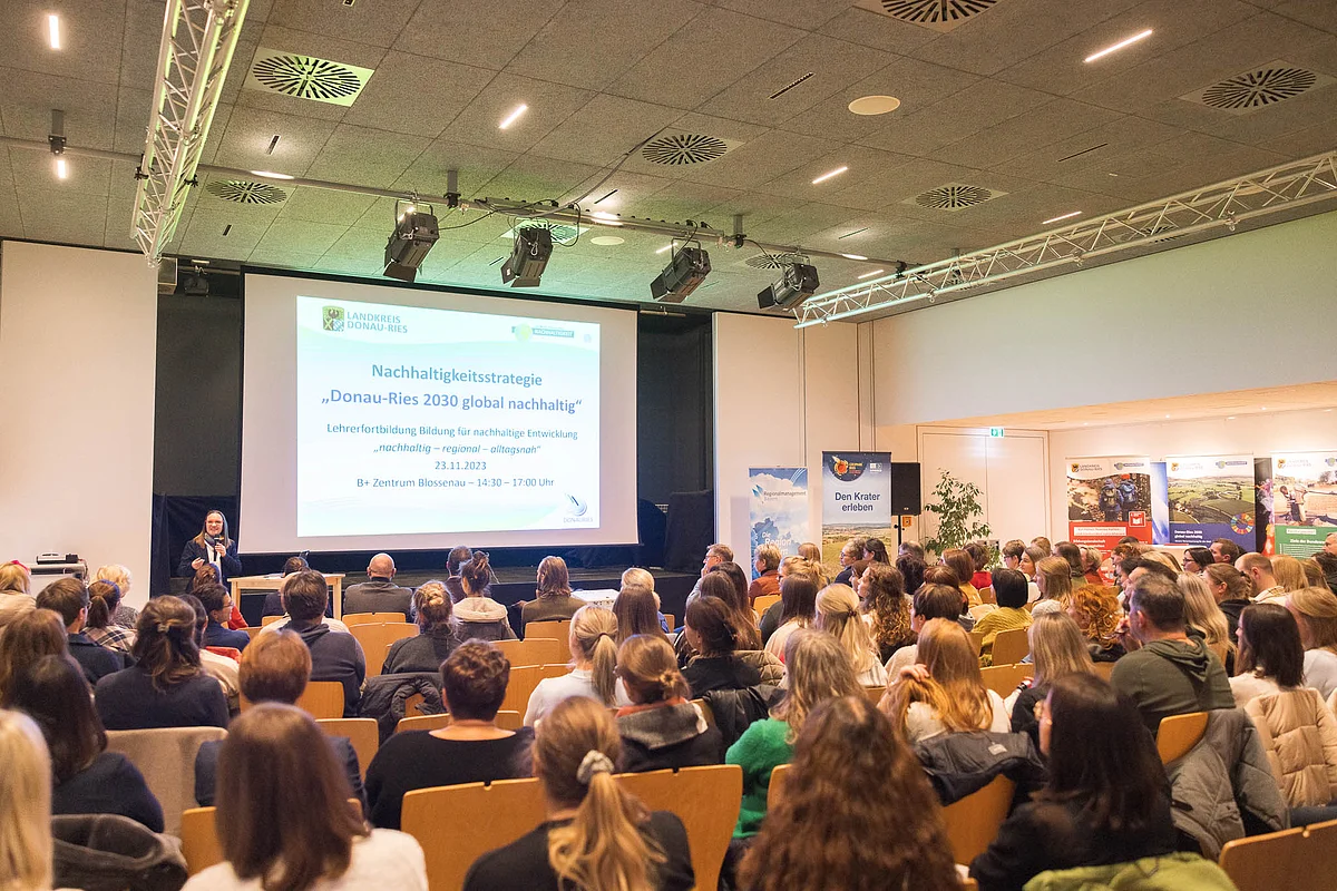 Auf einer Leinwand wird die Nachhaltigkeitsstrategie des Landkreises Donau-Ries präsentiert. Das Publikum sitzt auf Stuhlreihen.