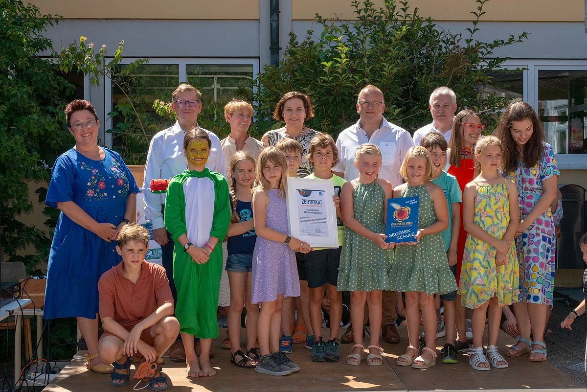 Gruppenbild mit Erwachsenen und Kindern, die das Zertifikat und das Schild "Geopark Ries Schule" in Händen halten.