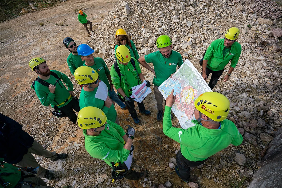 Eine Gruppe Personen in grünen Oberteilen und mit Helmen steht in einem Steinbruch und betrachtet eine geologische Karte.