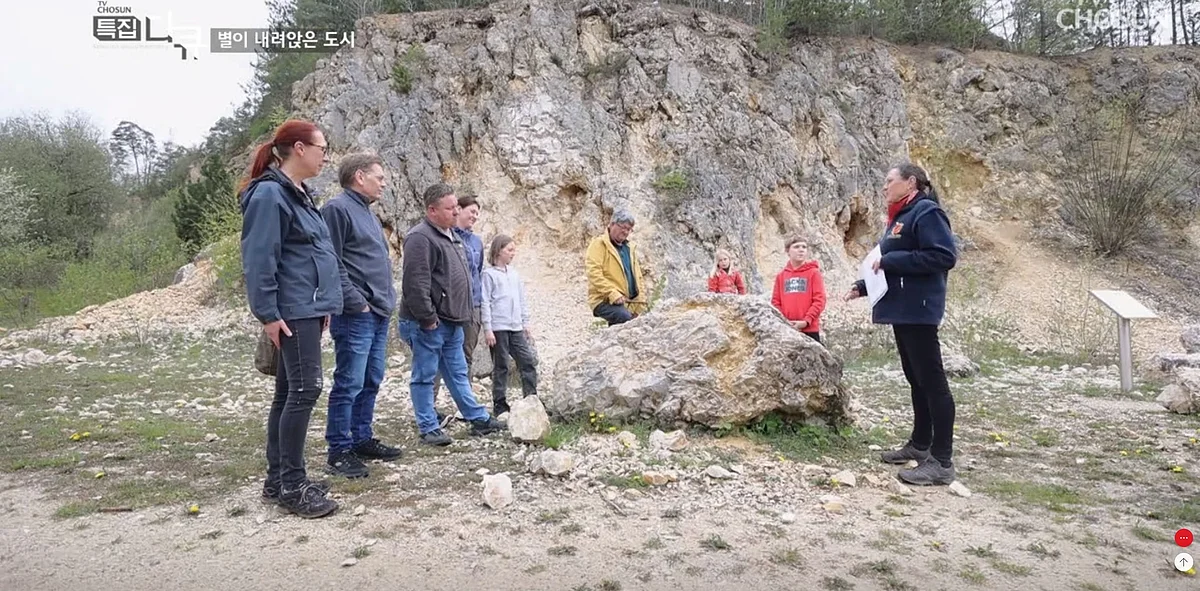 Eine Gruppe Personen steht um einen Gesteinsblock in einem ehemaligen Steinbruch.