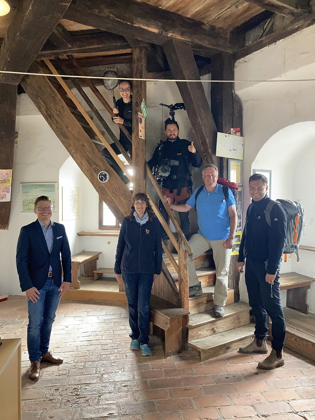 Mehrere Personen mit Filmequipment stehen auf einer steilen, alten Holztreppe. Am Fuß der Treppe ist der Bürgermeister der Stadt Nördlingen, David Wittner, zu sehen.