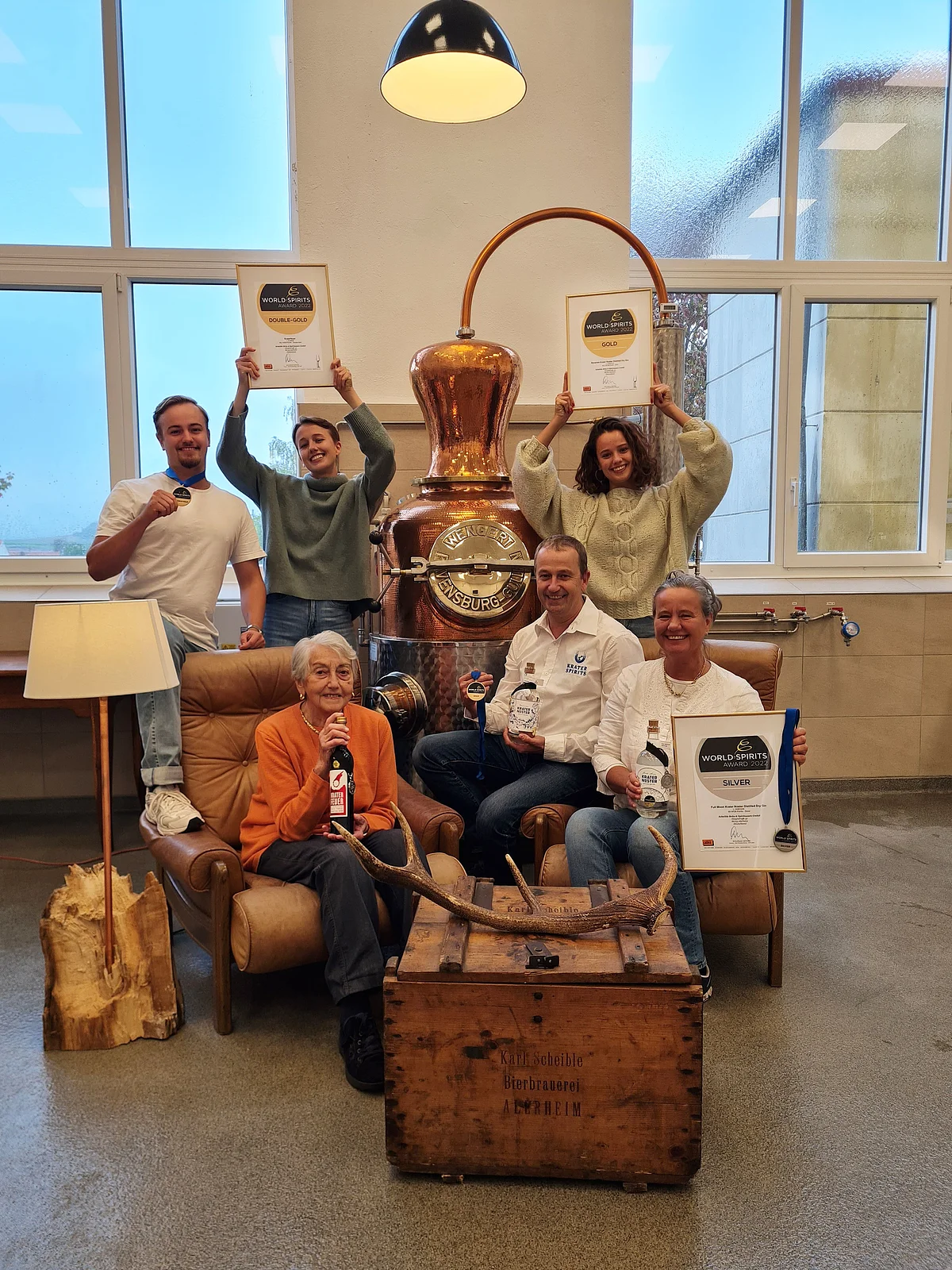 Eine Gruppe Personen steht um einen bronzenen Sudkessel und hält Bilderrahmen mit Urkunden in den Händen.