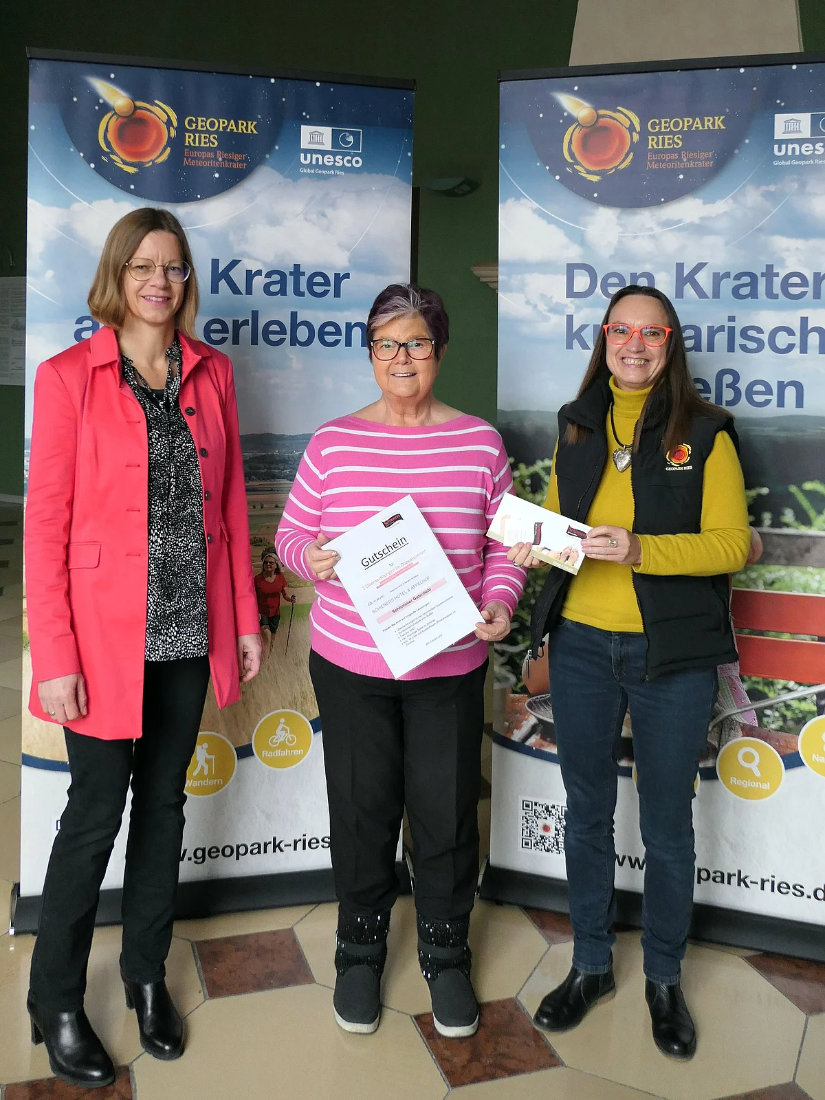 Drei Frauen stehen vor zwei großen Plakaten mit Logos des Geopark Ries.