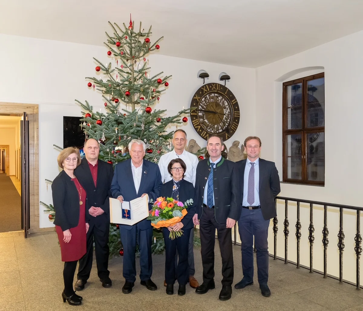 Eine Gruppe Personen steht vor einem weihnachtlich geschmückten Baum.