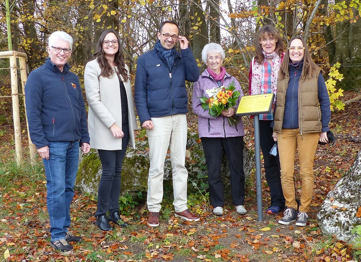 Günther Zwerger und Heike Burkhardt stehen mit weiteren Personen neben einer kleinen auf einem Pfosten befestigten gelben Tafel. Eine Frau hält einen Blumenstrauß in den Händen.