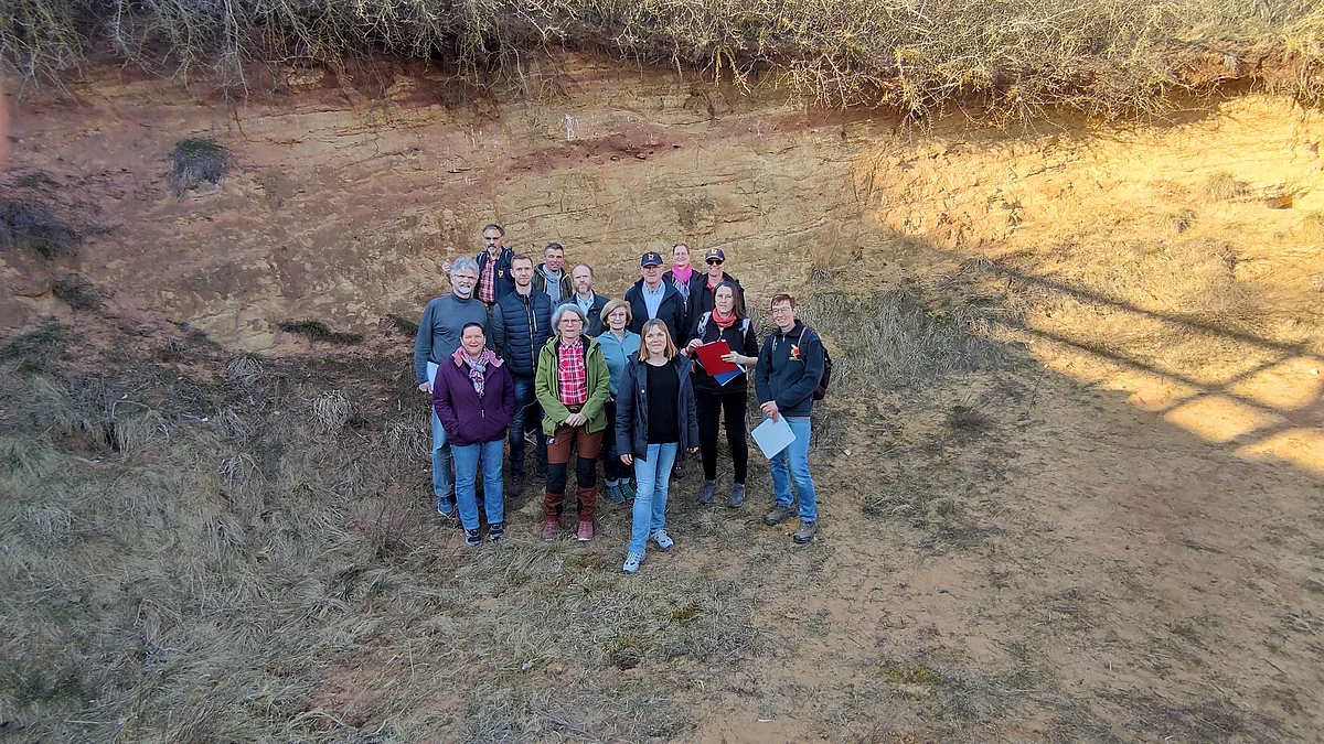 Eine Gruppe Personen steht in einer Grube mit rötlicher Felswand.