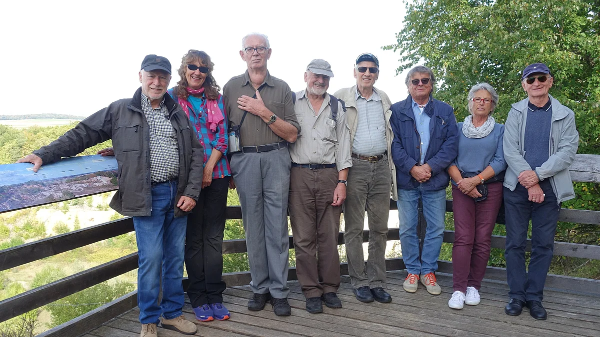 Eine Gruppe Personen steht auf einer Holzplattform. An der Brüstung ist eine Panoramatafel angebracht.