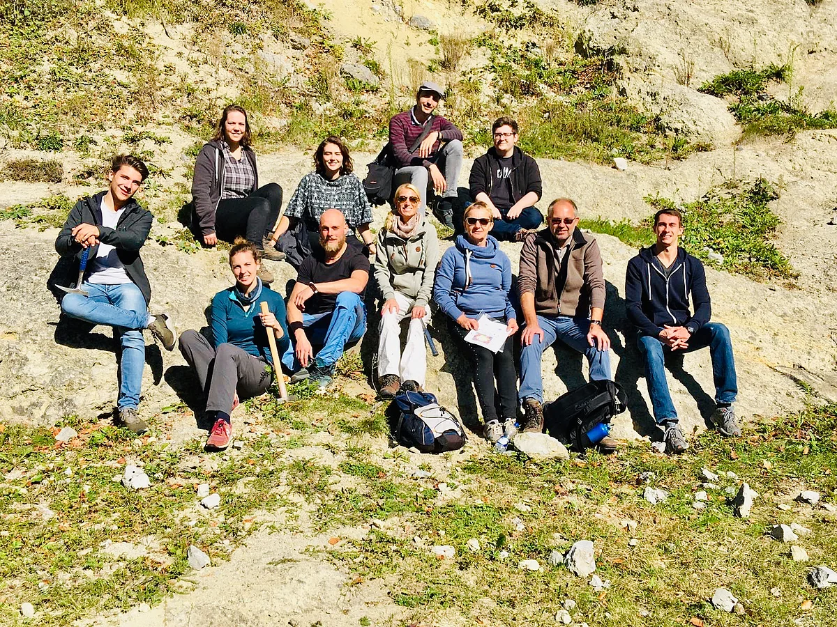 Eine Gruppe Personen sitzt an einem Hang mit mehreren Felsen.