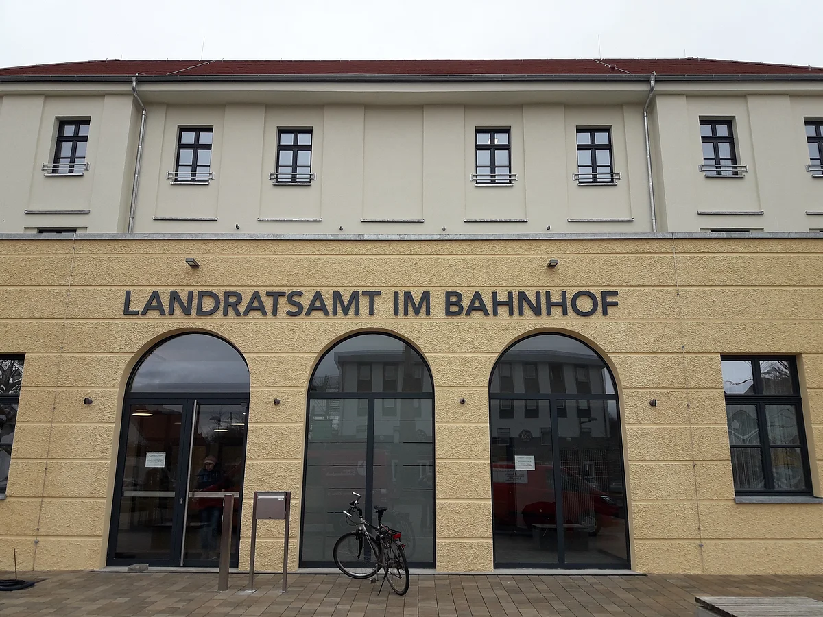 Der gelbe Vorbau eines Gebäudes trägt die Aufschrift "Landratsamt im Bahnhof" über den bogenförmigen Glasfenstern.