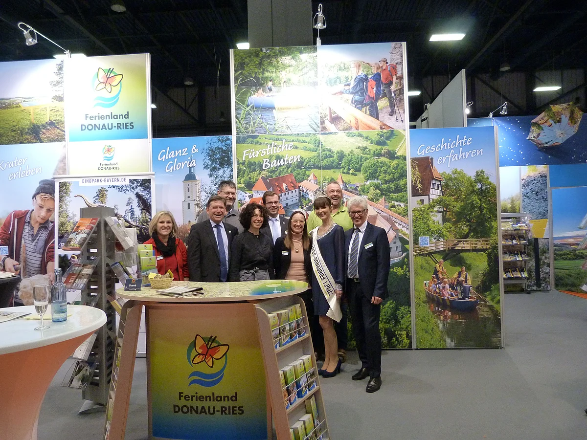 Eine Gruppe Personen steht zusammen mit der Miss "Donau-Ries" am Messestand des Ferienland Donau-Ries.