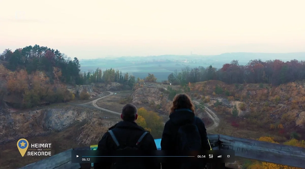 Zwei Personen blicken von einer Aussichtsplattform aus in einen ehemaligen Steinbruch.