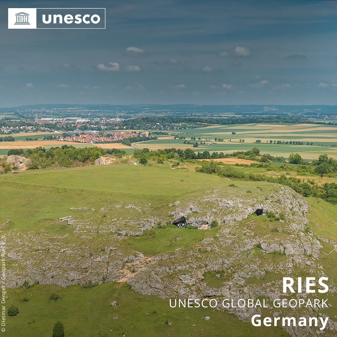 Hinter einem Hügel mit Wiese und Felsen erstreckt sich eine weite Landschaft mit Äckern und Siedlungen. Am Bildrand sind die Schriftzüge "UNESCO" und "UNESCO Global Geopark Ries Germany".
