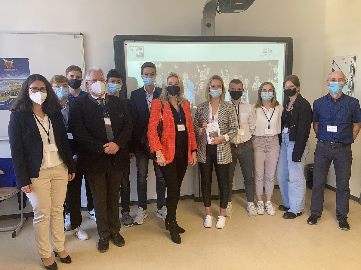 In einem Klassenzimmer stehen Kultusstaatssekretärin Anna Stolz und Vertreter:innen des THG Nördlingen. Alle Beteiligten tragen Mund-Nasen-Schutz.