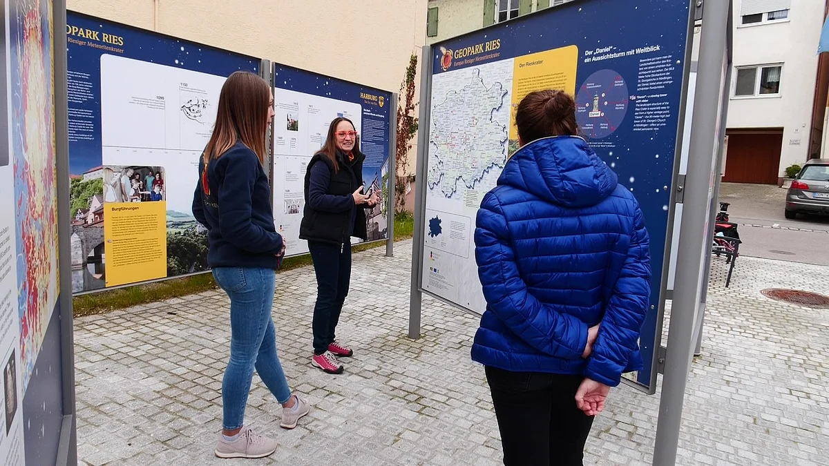 Drei Frauen stehen vor mehreren Informationstafeln über den Geopark Ries auf einem gepflasterten Platz.