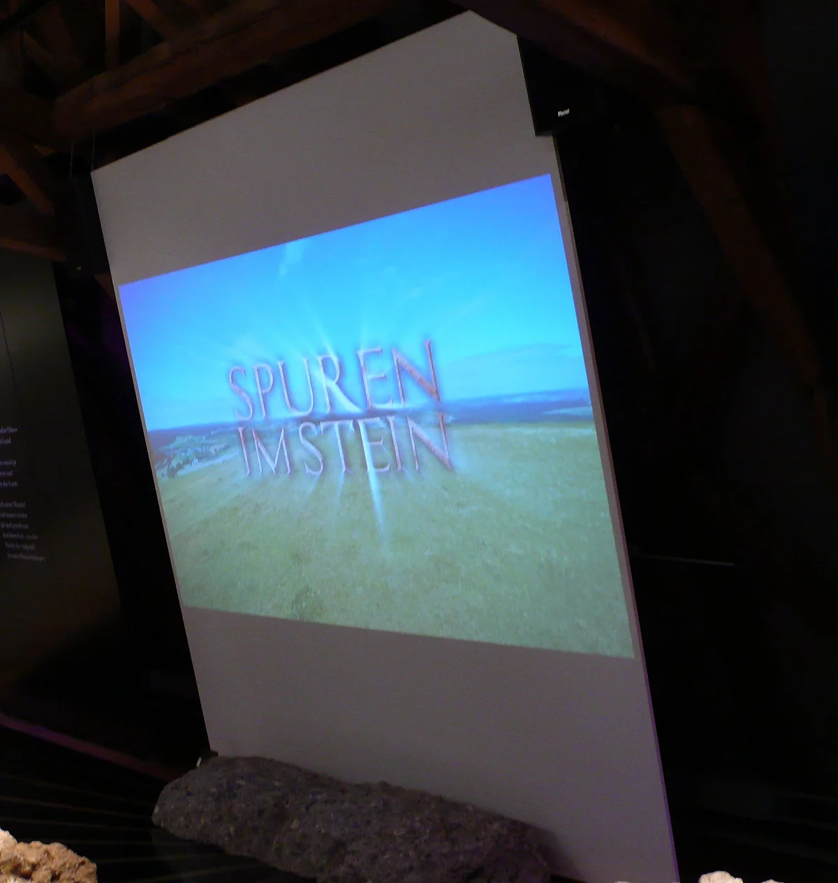 Eine Leinwand zeigt das Bild einer Landschaft und darüber den Schriftzug "Spuren im Stein".